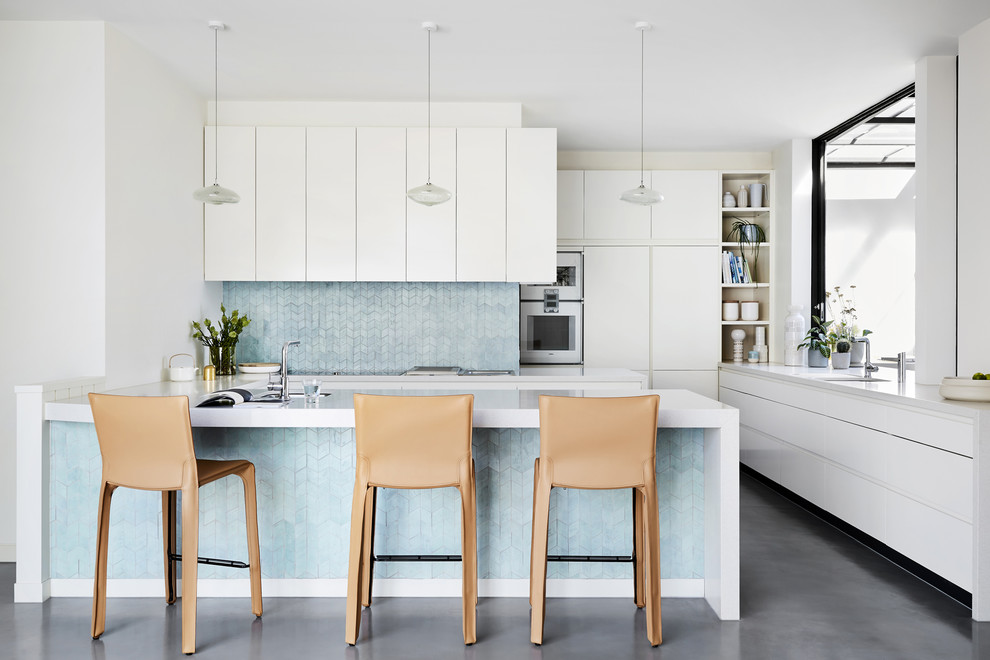 Contemporary u-shaped kitchen in Sydney with an undermount sink, flat-panel cabinets, white cabinets, blue splashback, white appliances, a peninsula, grey floor and white benchtop.