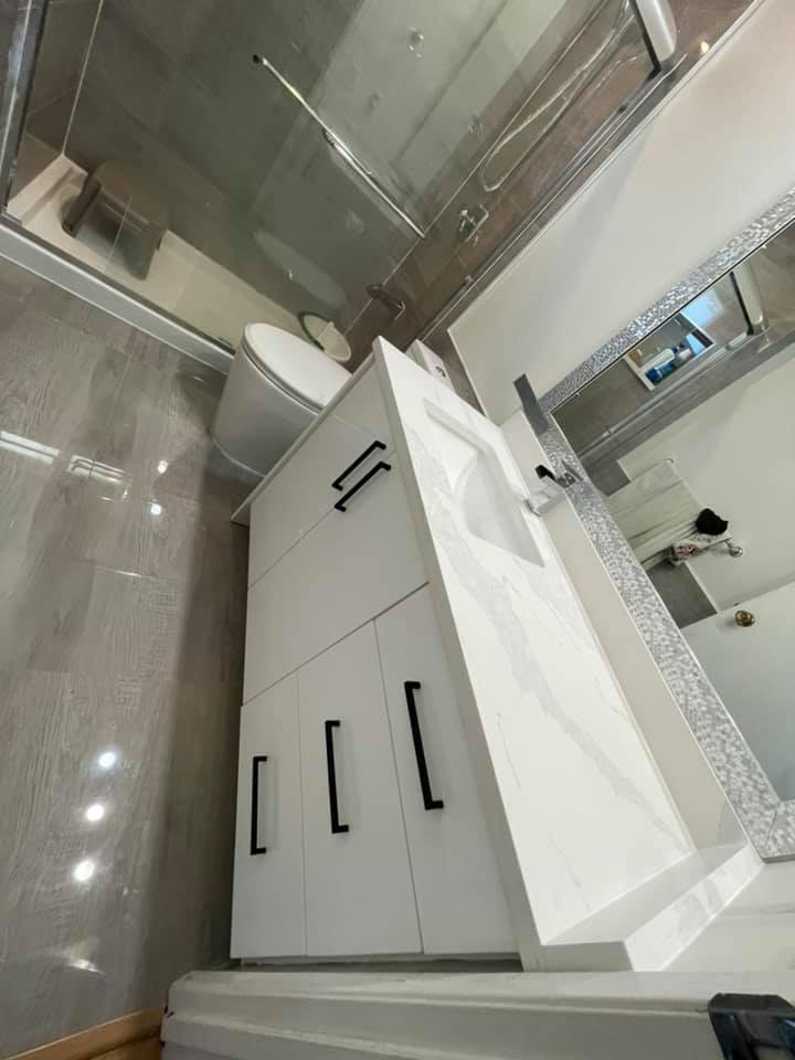 This is an example of a mid-sized modern master bathroom in Newark with furniture-like cabinets, white cabinets, a corner tub, a curbless shower, a one-piece toilet, white tile, limestone, black walls, ceramic floors, an undermount sink, brown floor, a hinged shower door, grey benchtops, an enclosed toilet, a single vanity, a freestanding vanity, timber and wood walls.