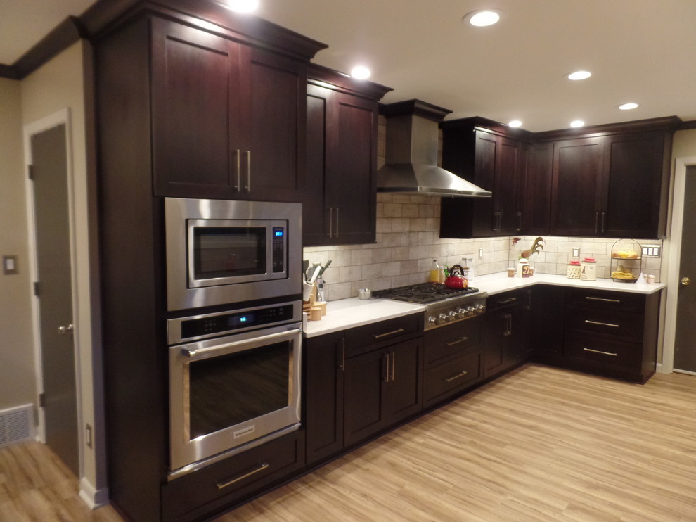 Eat-in kitchen - large transitional u-shaped laminate floor and beige floor eat-in kitchen idea with a farmhouse sink, shaker cabinets, dark wood cabinets, quartz countertops, gray backsplash, porcelain backsplash, stainless steel appliances and an island