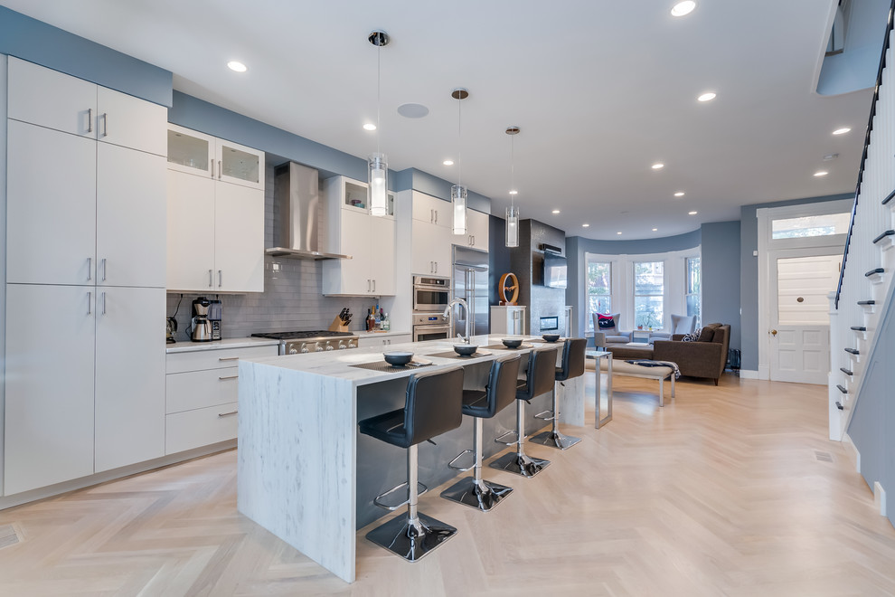 Photo of a mid-sized contemporary galley open plan kitchen in DC Metro with an undermount sink, flat-panel cabinets, white cabinets, quartz benchtops, white splashback, glass tile splashback, stainless steel appliances, light hardwood floors, with island, beige floor and white benchtop.