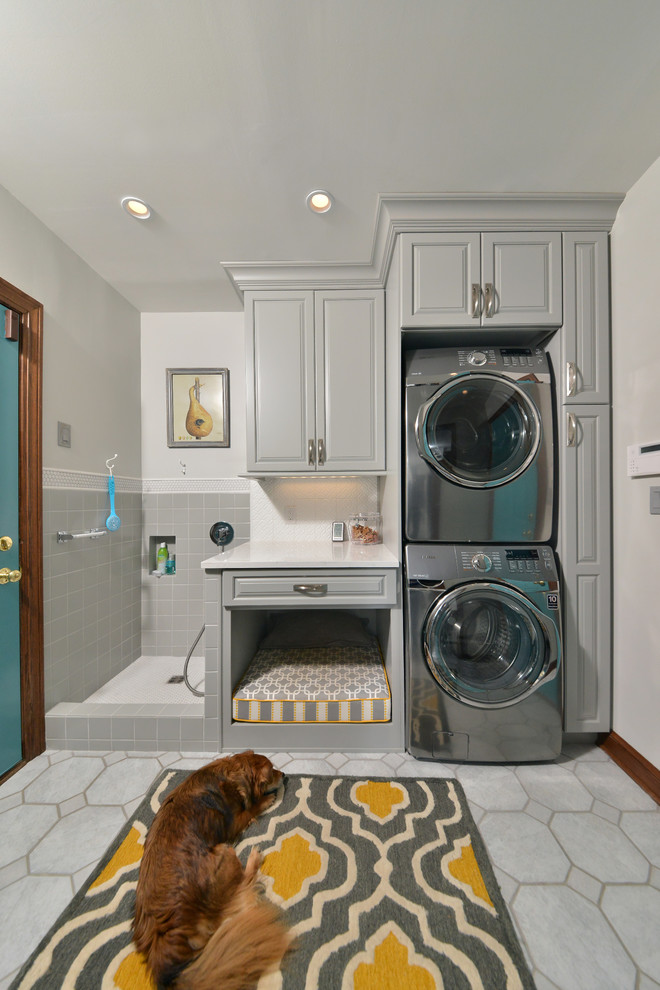 Mid-sized traditional single-wall utility room in Cleveland with an utility sink, raised-panel cabinets, grey cabinets, quartz benchtops, grey walls, porcelain floors, a stacked washer and dryer and grey floor.