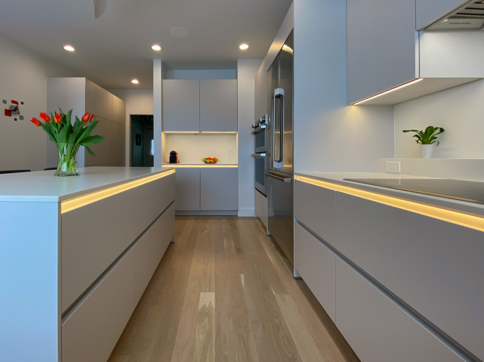 This is an example of a mid-sized contemporary u-shaped kitchen pantry in Boston with an undermount sink, flat-panel cabinets, grey cabinets, quartzite benchtops, white splashback, stone slab splashback, stainless steel appliances, light hardwood floors, with island, brown floor and white benchtop.