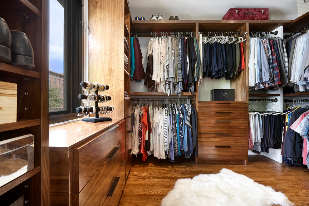 This is an example of a large contemporary gender-neutral walk-in wardrobe in New York with flat-panel cabinets, dark wood cabinets, light hardwood floors and brown floor.