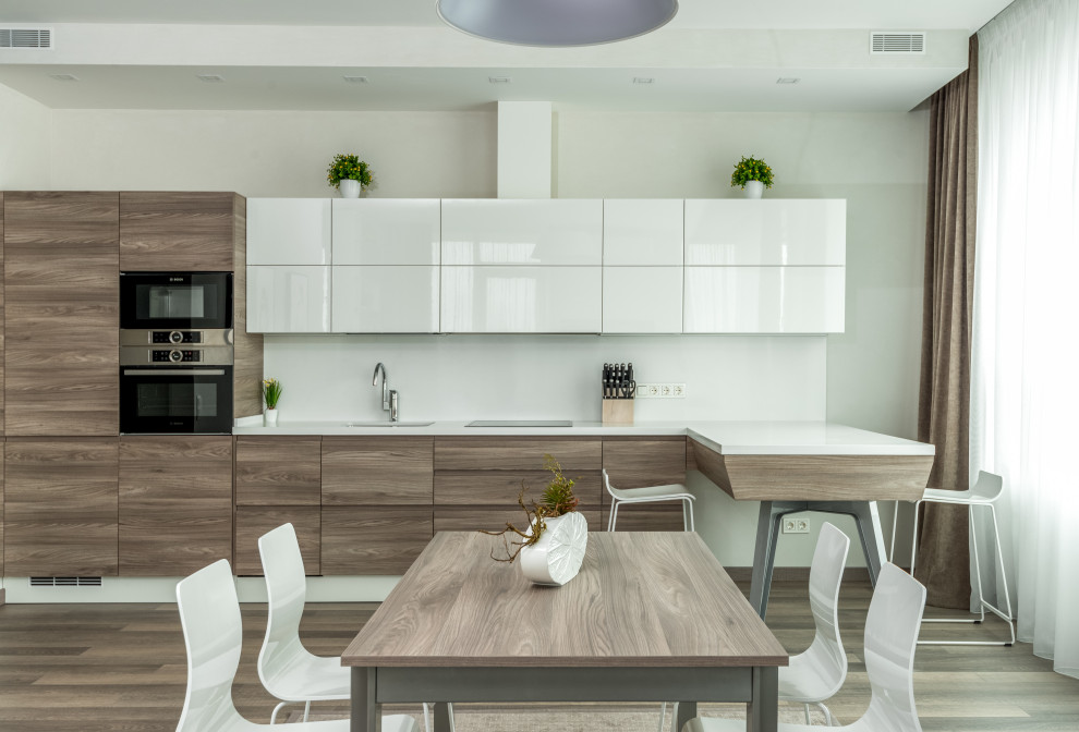 Design ideas for a large modern l-shaped kitchen/diner in Los Angeles with a built-in sink, flat-panel cabinets, white cabinets, wood worktops, white splashback, granite splashback, stainless steel appliances, light hardwood flooring, multiple islands and white worktops.