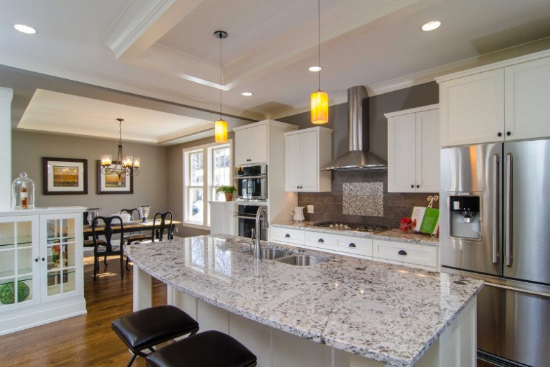 Open concept kitchen - transitional single-wall medium tone wood floor open concept kitchen idea in Minneapolis with a double-bowl sink, recessed-panel cabinets, white cabinets, granite countertops, stainless steel appliances, an island and gray backsplash