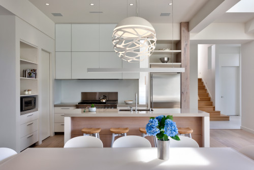 Bright minimalist kitchen with white handleless cabinets, wood-accent island, and sculptural pendant light