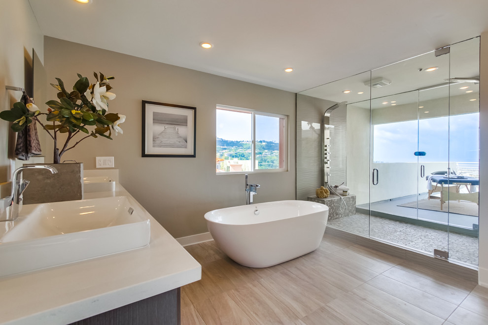 Photo of a large contemporary master bathroom in Denver with flat-panel cabinets, grey cabinets, a freestanding tub, a double shower, a one-piece toilet, a vessel sink, gray tile, pebble tile, grey walls, quartzite benchtops, porcelain floors, beige floor and a hinged shower door.