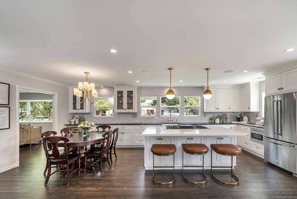 This is an example of a large transitional l-shaped open plan kitchen in San Francisco with a farmhouse sink, white cabinets, quartz benchtops, white splashback, subway tile splashback, stainless steel appliances, with island, brown floor, white benchtop, recessed-panel cabinets and dark hardwood floors.