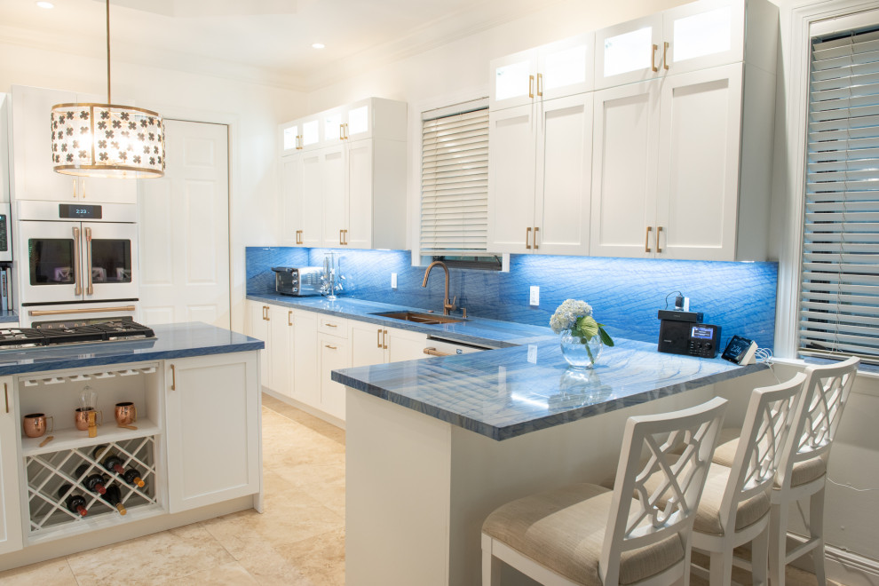 Photo of a mid-sized traditional u-shaped eat-in kitchen in Miami with an undermount sink, shaker cabinets, white cabinets, blue splashback, white appliances, with island and blue benchtop.