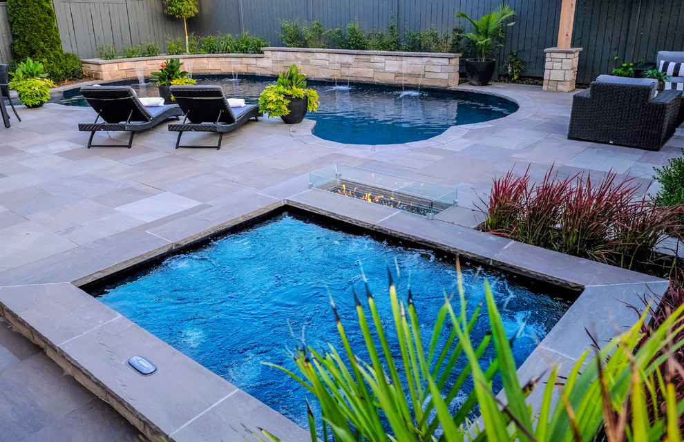Photo of a small transitional backyard kidney-shaped pool in Toronto with a hot tub and natural stone pavers.