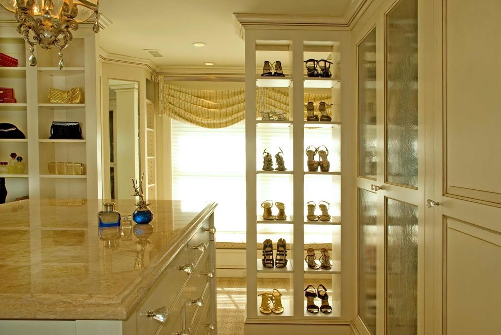 This is an example of a large women's walk-in wardrobe in New York with glass-front cabinets, beige cabinets and carpet.