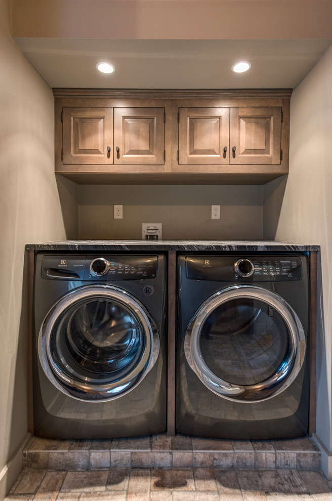 Inspiration for a small traditional single-wall dedicated laundry room in Boston with raised-panel cabinets, medium wood cabinets, beige walls, ceramic floors, a side-by-side washer and dryer, brown floor and black benchtop.