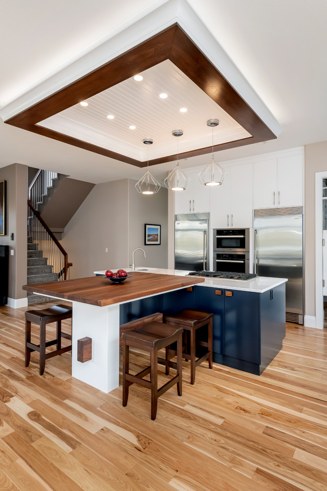 Large transitional l-shaped light wood floor and beige floor kitchen pantry photo with a double-bowl sink, flat-panel cabinets, white cabinets, quartz countertops, gray backsplash, cement tile backsplash, stainless steel appliances, an island and white countertops