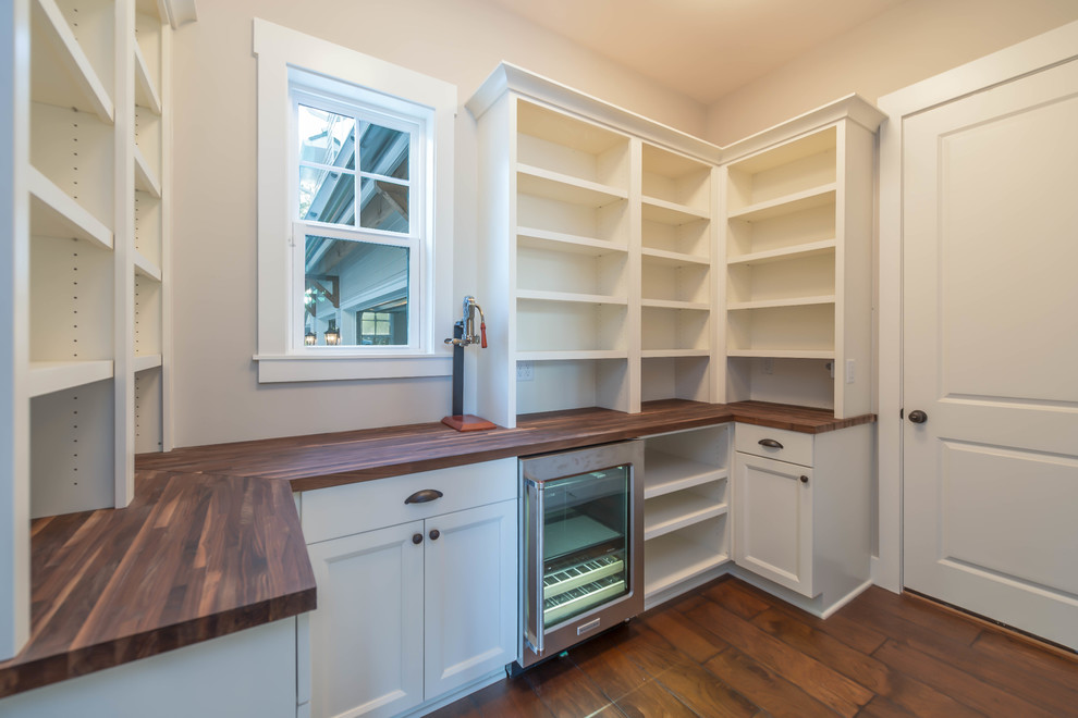 Inspiration for a mid-sized beach style l-shaped wet bar in Jacksonville with no sink, recessed-panel cabinets, white cabinets, wood benchtops and ceramic floors.