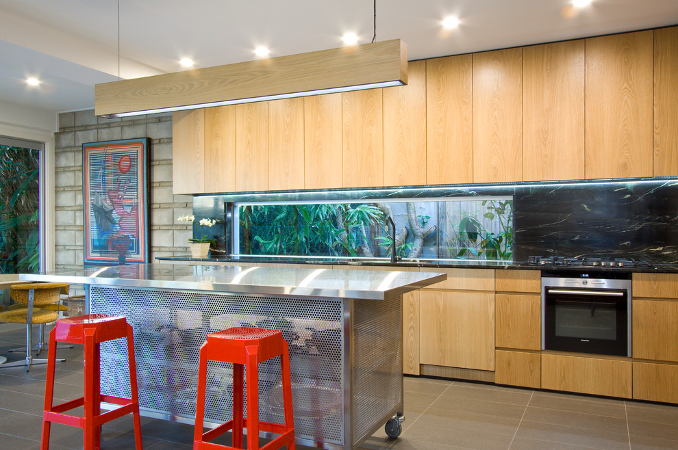 This is an example of a contemporary galley kitchen in Sunshine Coast with flat-panel cabinets, medium wood cabinets, window splashback, stainless steel appliances, with island, grey floor and black benchtop.