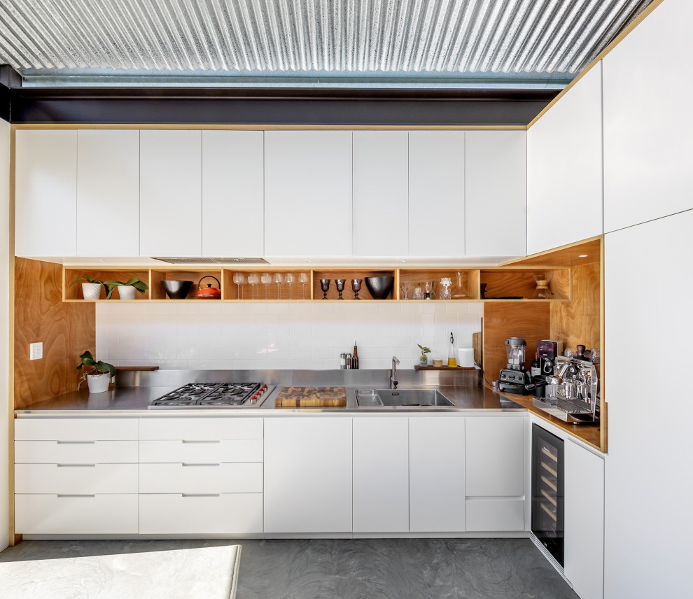 This is an example of a contemporary l-shaped kitchen in Sydney with an integrated sink, flat-panel cabinets, white cabinets, stainless steel benchtops, no island, grey floor and grey benchtop.