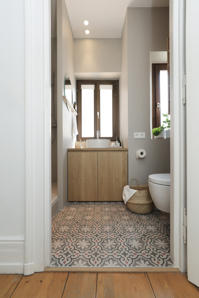 Design ideas for a small modern 3/4 bathroom in Frankfurt with flat-panel cabinets, light wood cabinets, an alcove shower, a two-piece toilet, gray tile, grey walls, cement tiles, a vessel sink, wood benchtops, multi-coloured floor, an open shower, a single vanity, a built-in vanity, wallpaper and wallpaper.