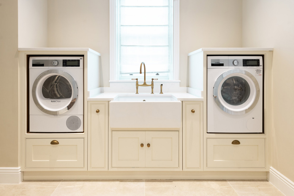 Inspiration for a large classic galley utility room in Hertfordshire with a belfast sink, shaker cabinets, white cabinets, quartz worktops, white walls, ceramic flooring, an integrated washer and dryer, beige floors, white worktops and a feature wall.