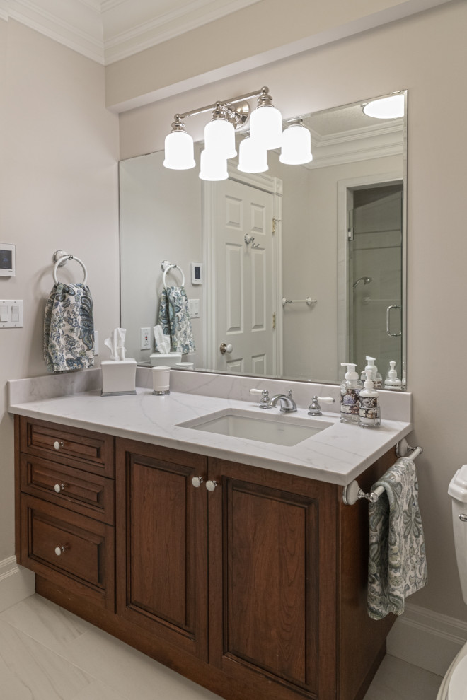 Mid-sized traditional master bathroom in Edmonton with furniture-like cabinets, dark wood cabinets, a freestanding tub, an alcove shower, a two-piece toilet, white tile, cement tile, beige walls, marble floors, an undermount sink, engineered quartz benchtops, white floor, a hinged shower door, white benchtops, a shower seat, a double vanity and a freestanding vanity.