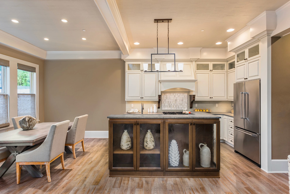 Example of a mid-sized transitional l-shaped light wood floor and beige floor eat-in kitchen design with raised-panel cabinets, white cabinets, stainless steel appliances, an island and gray countertops