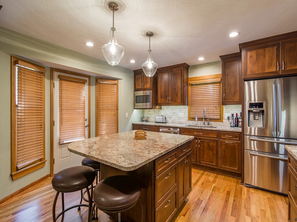 This is an example of a mid-sized traditional l-shaped separate kitchen in Kansas City with an undermount sink, flat-panel cabinets, brown cabinets, granite benchtops, beige splashback, stone tile splashback, stainless steel appliances, light hardwood floors and with island.