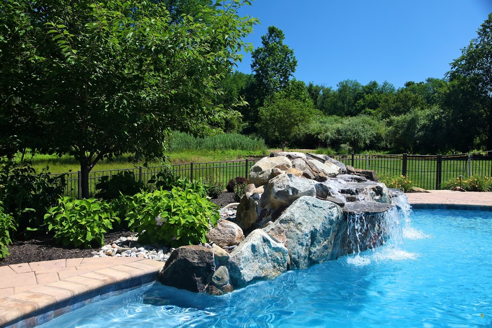Mid-sized country backyard custom-shaped pool in New York with a water feature and brick pavers.