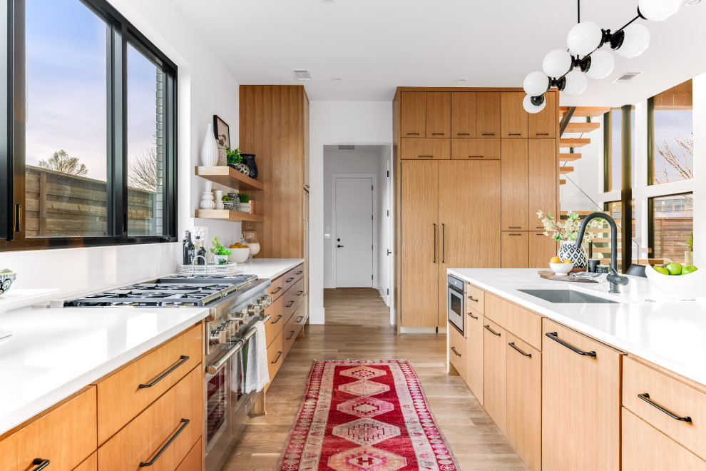 This is an example of a large midcentury open plan kitchen in Dallas with a submerged sink, flat-panel cabinets, light wood cabinets, engineered stone countertops, white splashback, engineered quartz splashback, integrated appliances, light hardwood flooring, an island, brown floors and white worktops.