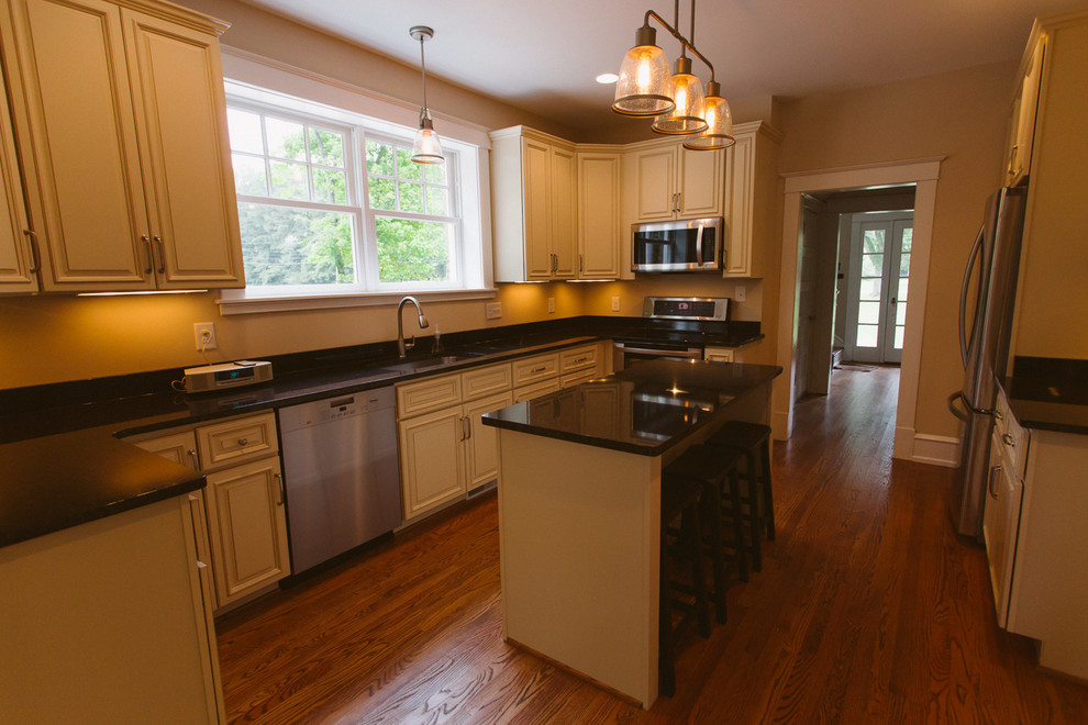 Large arts and crafts eat-in kitchen in Other with an undermount sink, raised-panel cabinets, beige cabinets, solid surface benchtops, stainless steel appliances, medium hardwood floors and with island.