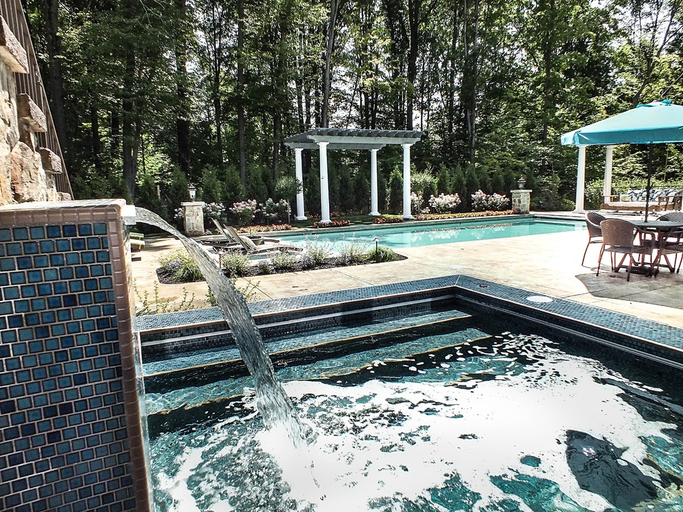 This is an example of a large modern backyard rectangular pool in Cleveland with concrete pavers and a water feature.