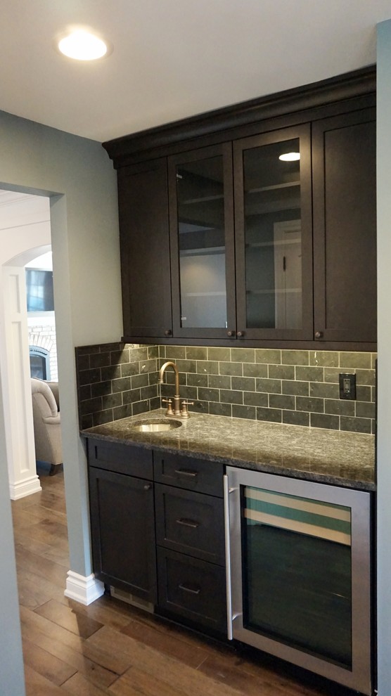 This is an example of a mid-sized contemporary single-wall wet bar in Detroit with an undermount sink, shaker cabinets, dark wood cabinets, granite benchtops, green splashback, subway tile splashback, medium hardwood floors and brown floor.
