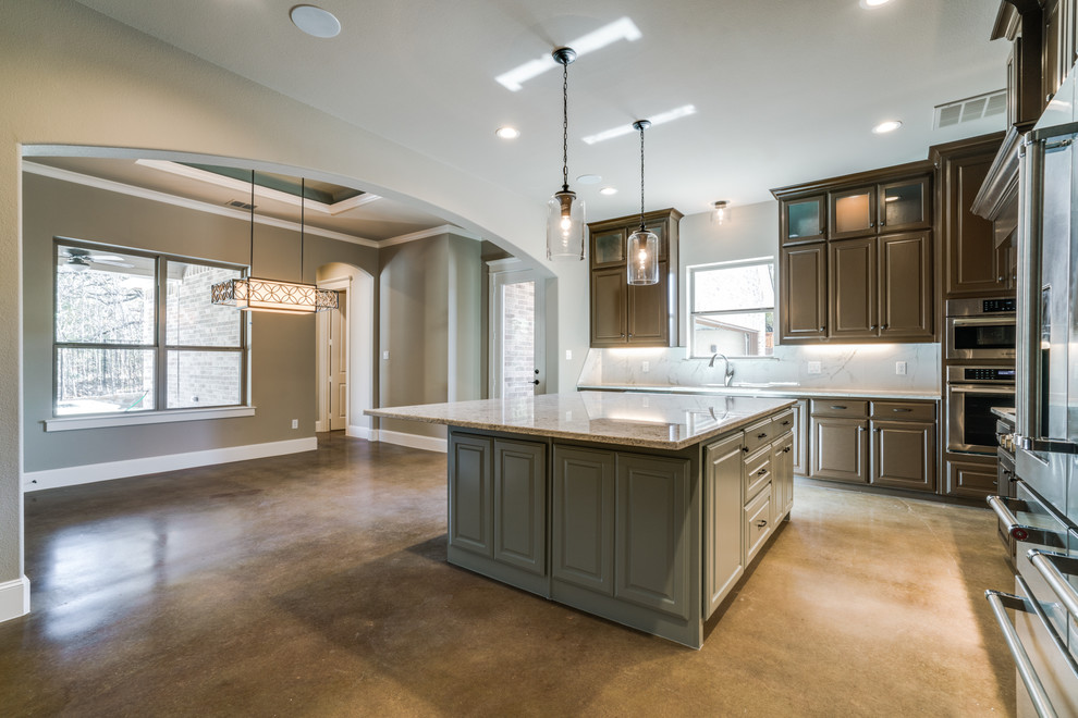 This is an example of a large transitional l-shaped kitchen in Dallas with an undermount sink, raised-panel cabinets, brown cabinets, granite benchtops, white splashback, ceramic splashback, stainless steel appliances, concrete floors and with island.