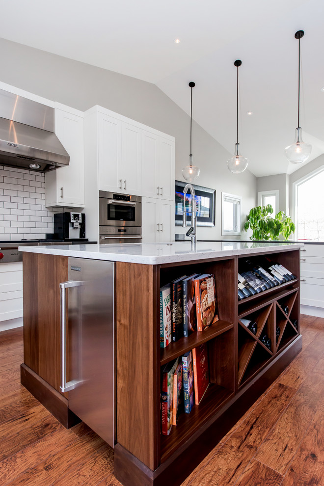 Large transitional u-shaped medium tone wood floor kitchen pantry photo in Calgary with a single-bowl sink, shaker cabinets, white cabinets, quartz countertops, white backsplash, subway tile backsplash, stainless steel appliances and an island