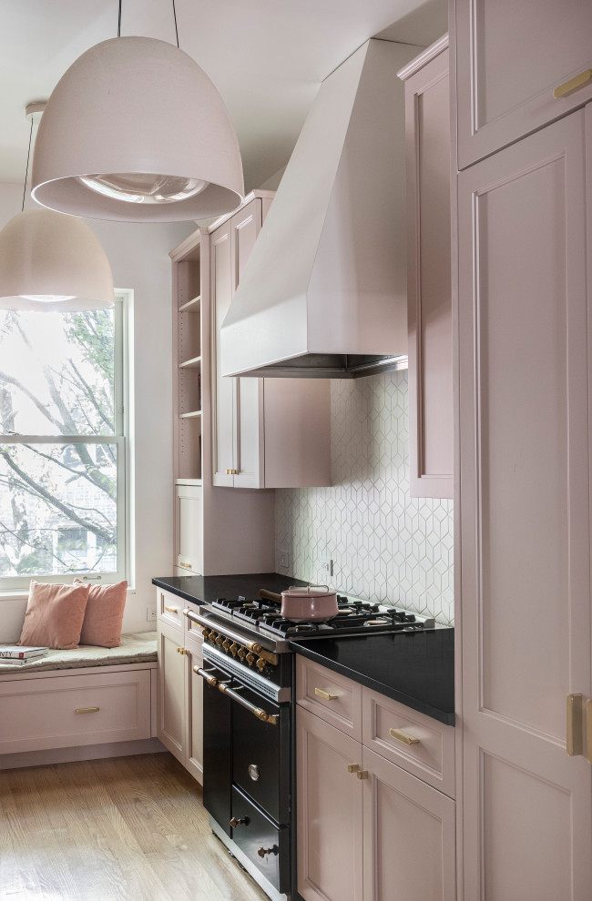 This is an example of a small transitional galley separate kitchen in New York with an undermount sink, recessed-panel cabinets, pink cabinets, soapstone benchtops, white splashback, ceramic splashback, panelled appliances, light hardwood floors and black benchtop.