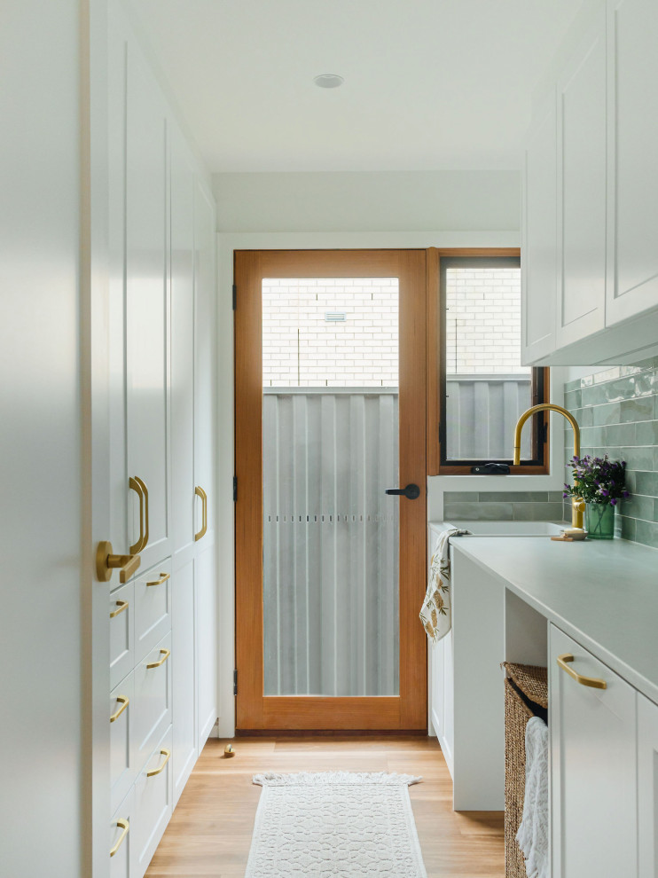 Inspiration for a mid-sized transitional galley dedicated laundry room in Melbourne with a single-bowl sink, shaker cabinets, white cabinets, laminate benchtops, green splashback, subway tile splashback, white walls, vinyl floors, a side-by-side washer and dryer, brown floor and grey benchtop.