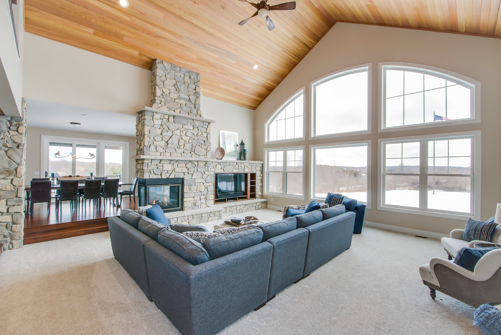 Inspiration for a large country open concept family room in Grand Rapids with beige walls, carpet, a two-sided fireplace, a stone fireplace surround, a built-in media wall and beige floor.