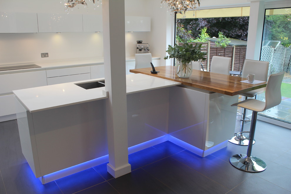 Photo of a mid-sized modern eat-in kitchen in Hertfordshire with an undermount sink, flat-panel cabinets, white cabinets, quartz benchtops, stainless steel appliances, porcelain floors and with island.