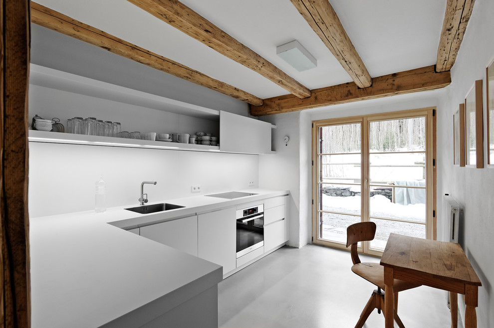 Design ideas for a small contemporary l-shaped separate kitchen in Stuttgart with a drop-in sink, flat-panel cabinets, white cabinets, white splashback, black appliances and linoleum floors.