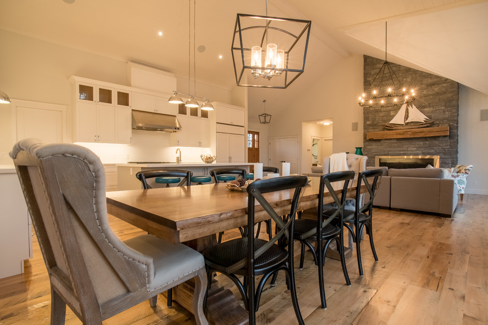 This is an example of a mid-sized transitional open plan dining in Toronto with white walls, light hardwood floors and a stone fireplace surround.