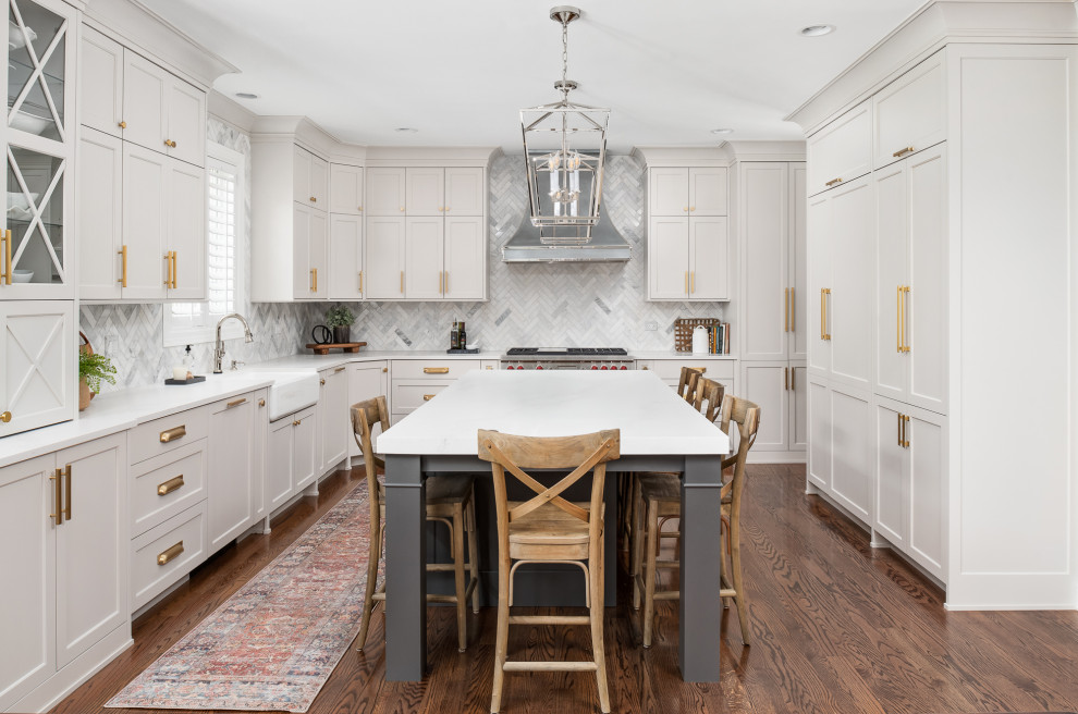 This is an example of a large transitional u-shaped eat-in kitchen in Chicago with a farmhouse sink, shaker cabinets, white cabinets, quartzite benchtops, grey splashback, marble splashback, stainless steel appliances, dark hardwood floors, with island, brown floor and white benchtop.