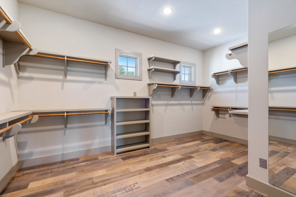 Large country gender-neutral walk-in wardrobe in Austin with shaker cabinets, grey cabinets, light hardwood floors and grey floor.