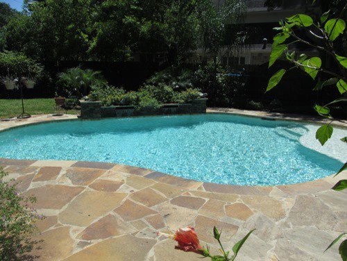 This is an example of a mid-sized contemporary backyard custom-shaped pool in Houston with natural stone pavers.
