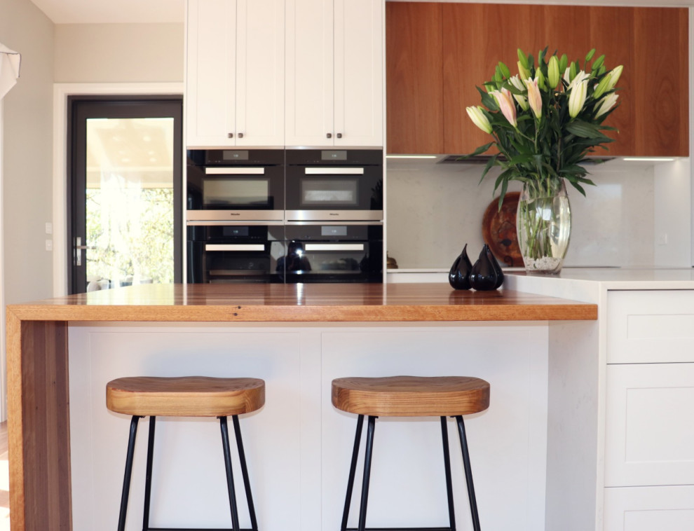 Inspiration for a mid-sized contemporary l-shaped eat-in kitchen in Canberra - Queanbeyan with a double-bowl sink, shaker cabinets, white cabinets, quartz benchtops, white splashback, stone slab splashback, black appliances, dark hardwood floors, with island, multi-coloured floor and white benchtop.