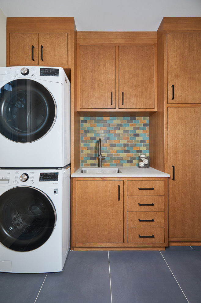 Inredning av en amerikansk mellanstor vita linjär vitt tvättstuga enbart för tvätt, med en undermonterad diskho, släta luckor, skåp i mellenmörkt trä, bänkskiva i kvarts, flerfärgad stänkskydd, klinkergolv i keramik, en tvättpelare och grått golv