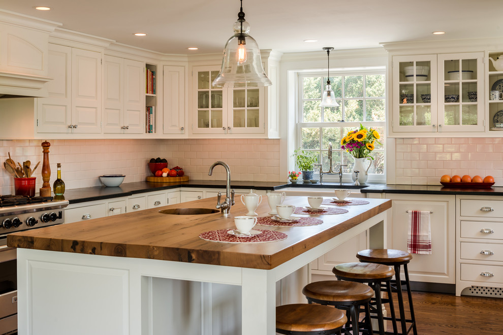 Large country u-shaped eat-in kitchen in Philadelphia with a farmhouse sink, white cabinets, white splashback, subway tile splashback, stainless steel appliances, medium hardwood floors, with island, wood benchtops, brown floor, black benchtop and beaded inset cabinets.
