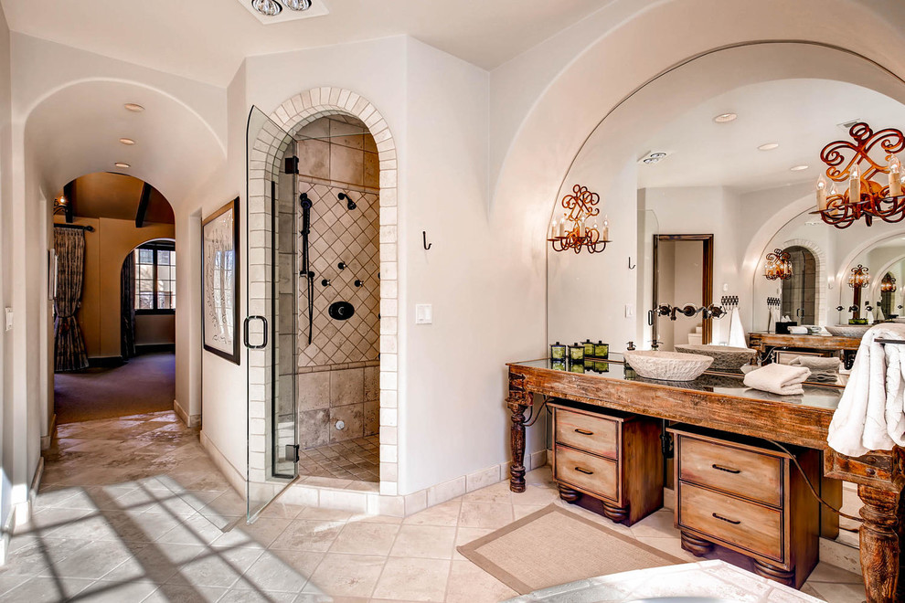 Inspiration for a mid-sized mediterranean master bathroom in Denver with distressed cabinets, a corner shower, beige tile, stone tile, beige walls, travertine floors, a vessel sink and glass benchtops.