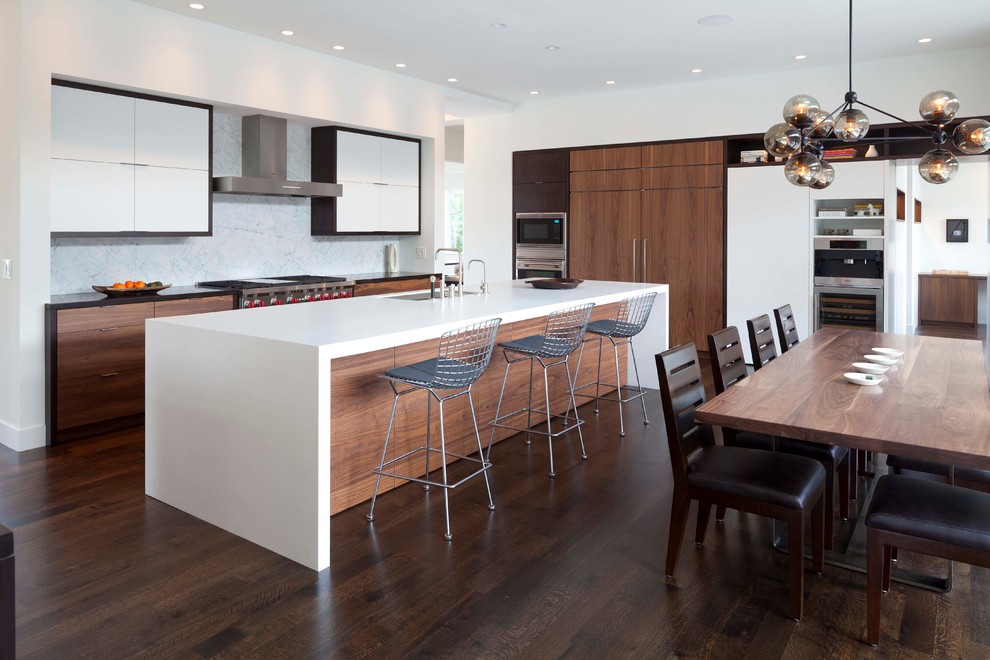 Photo of a contemporary l-shaped eat-in kitchen in Minneapolis with an undermount sink, flat-panel cabinets, solid surface benchtops, white splashback, stone slab splashback, stainless steel appliances and white cabinets.