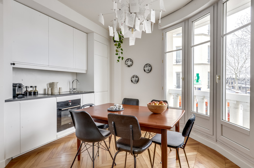 Inspiration for a scandinavian single-wall eat-in kitchen in Paris with a drop-in sink, flat-panel cabinets, white cabinets, white splashback, black appliances, medium hardwood floors, no island, brown floor and black benchtop.