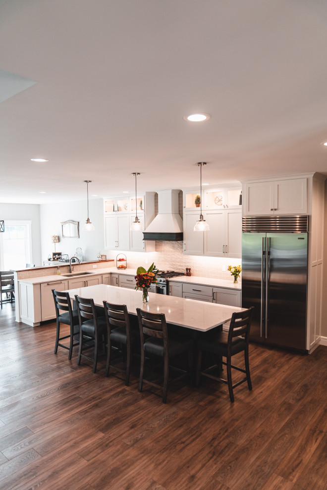Kitchen pantry - large transitional l-shaped vinyl floor and brown floor kitchen pantry idea with an undermount sink, shaker cabinets, white cabinets, quartz countertops, gray backsplash, subway tile backsplash, stainless steel appliances, an island and white countertops