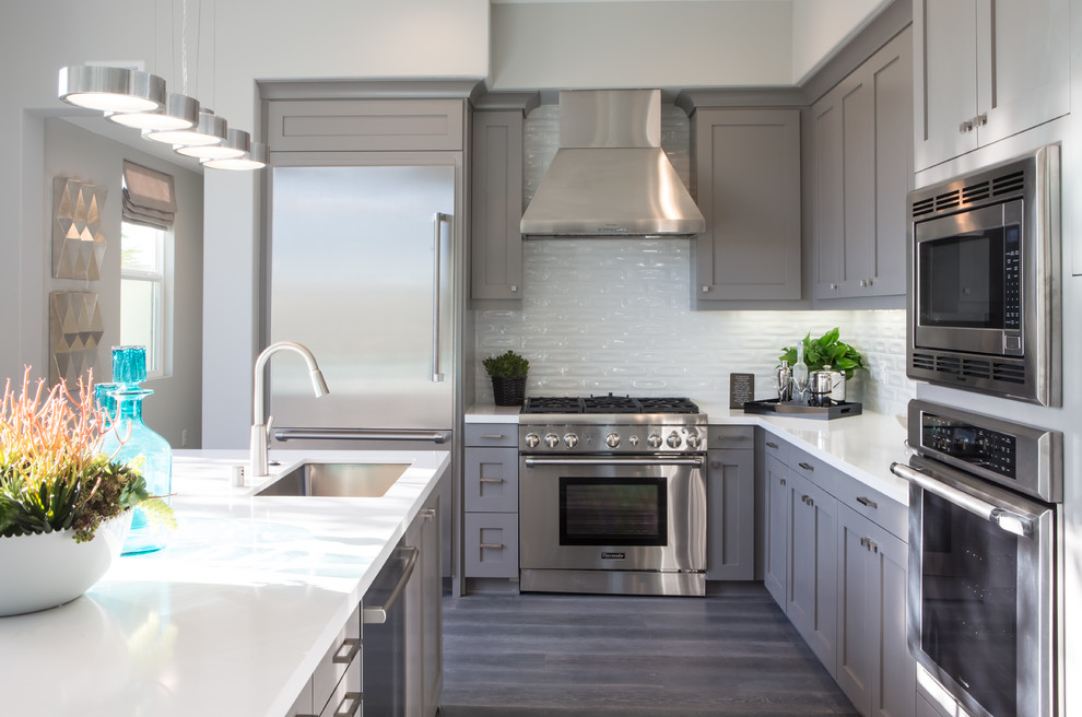 Inspiration for a contemporary l-shaped open plan kitchen in Orange County with an undermount sink, shaker cabinets, grey cabinets, quartz benchtops, white splashback, stainless steel appliances, light hardwood floors and with island.