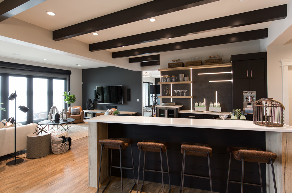 Inspiration for a large country single-wall seated home bar in Calgary with an undermount sink, flat-panel cabinets, black cabinets, quartz benchtops, black splashback, porcelain splashback, vinyl floors, brown floor and white benchtop.